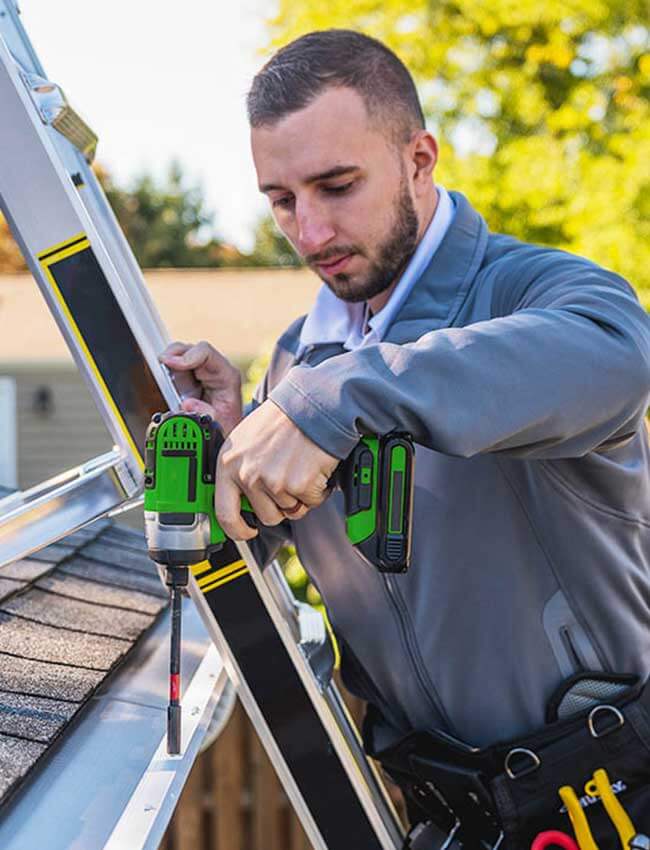 leaf filter gutter installer standing on a ladder while using a drill
