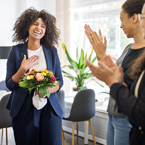 a woman receives flowers followed by an applause from coworkers