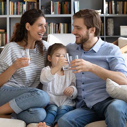 two parents and their child sitting on a couch drinking water
