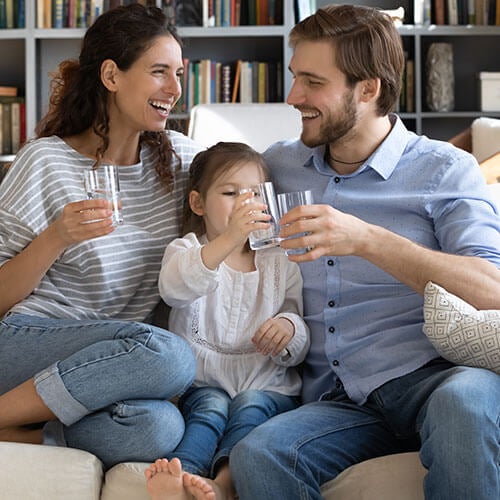 parents and young daughter sitting on couch drinking water