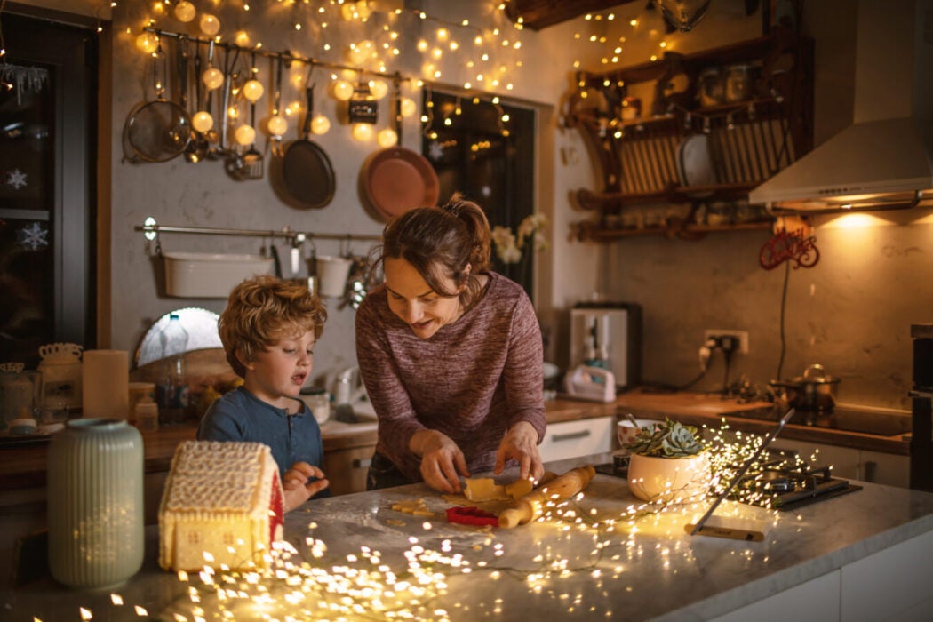 Boy and woman making cookies in kitchen with twinkle lights