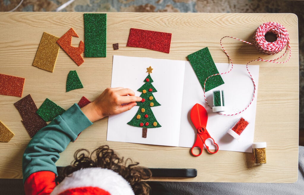 Kid crafting Christmas card with felt decoration cutouts on table