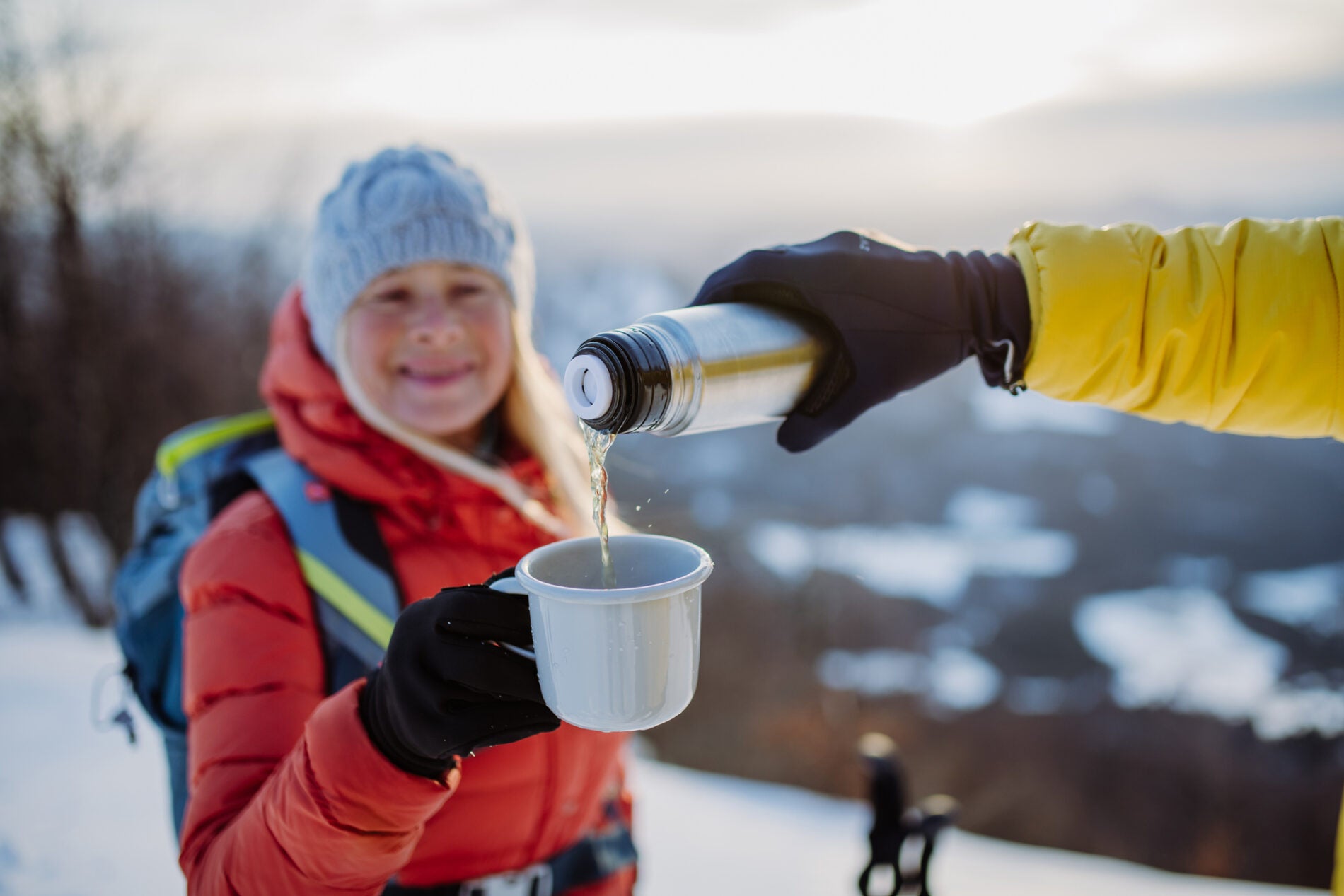 Couple hiking in winter, drinking hot tea. Close up pouring tea in mug.