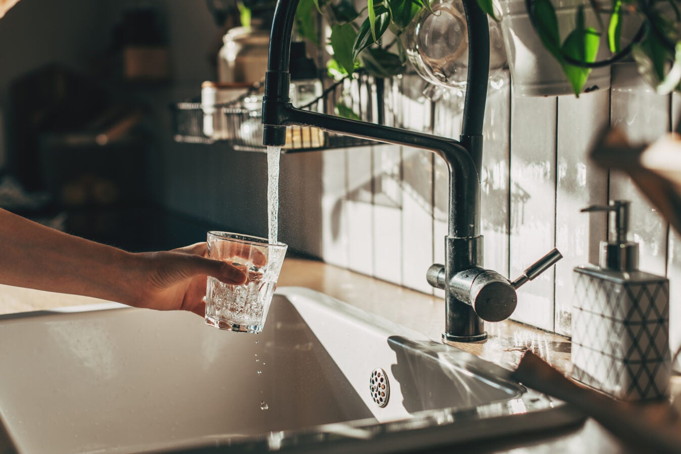 Woman filling glass with tap water from tap in kitchen, closeup